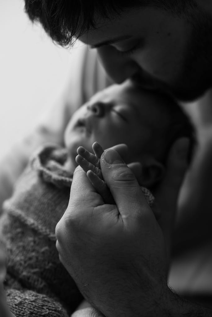 A father gently kisses his sleeping newborn, capturing the serene bond and love.