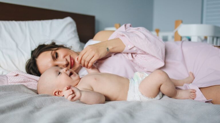 Jeune maman allongée sur le lit auprès de son bébé