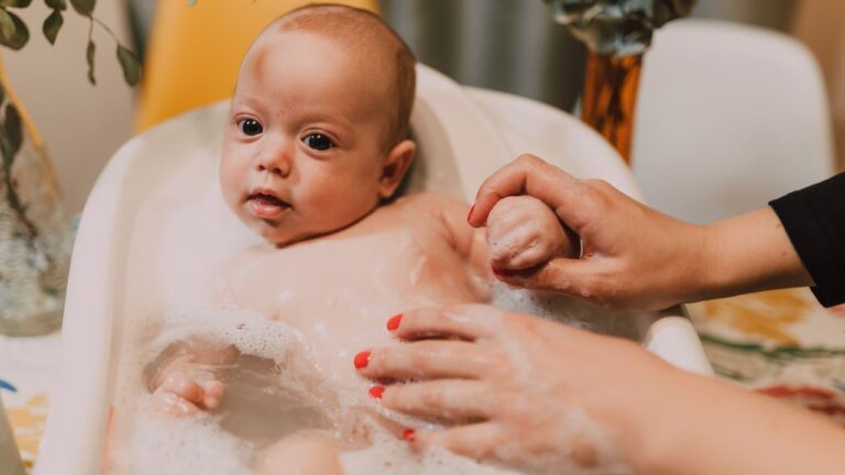 Bébé qui prend son premier bain, lavé délicatement par les mains de sa maman